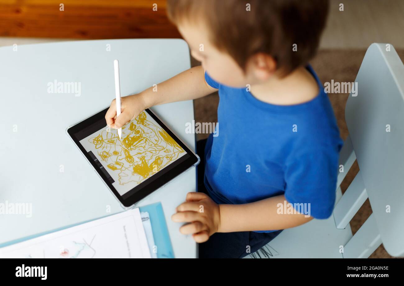 Cute boy in blue t shirt using digital tablet or computer for drawing ...