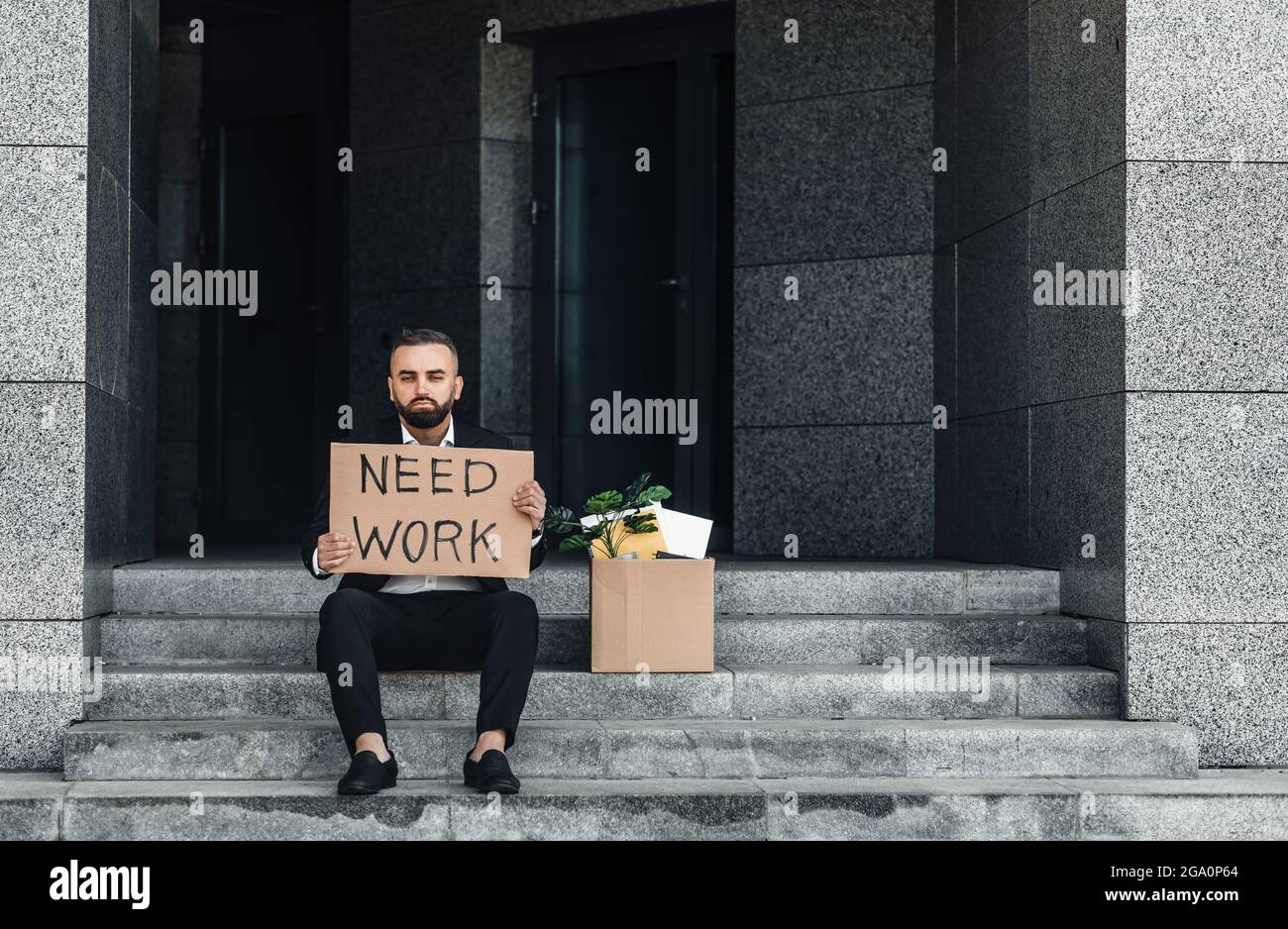Laid off male office worker sitting near box with belongings on stairs