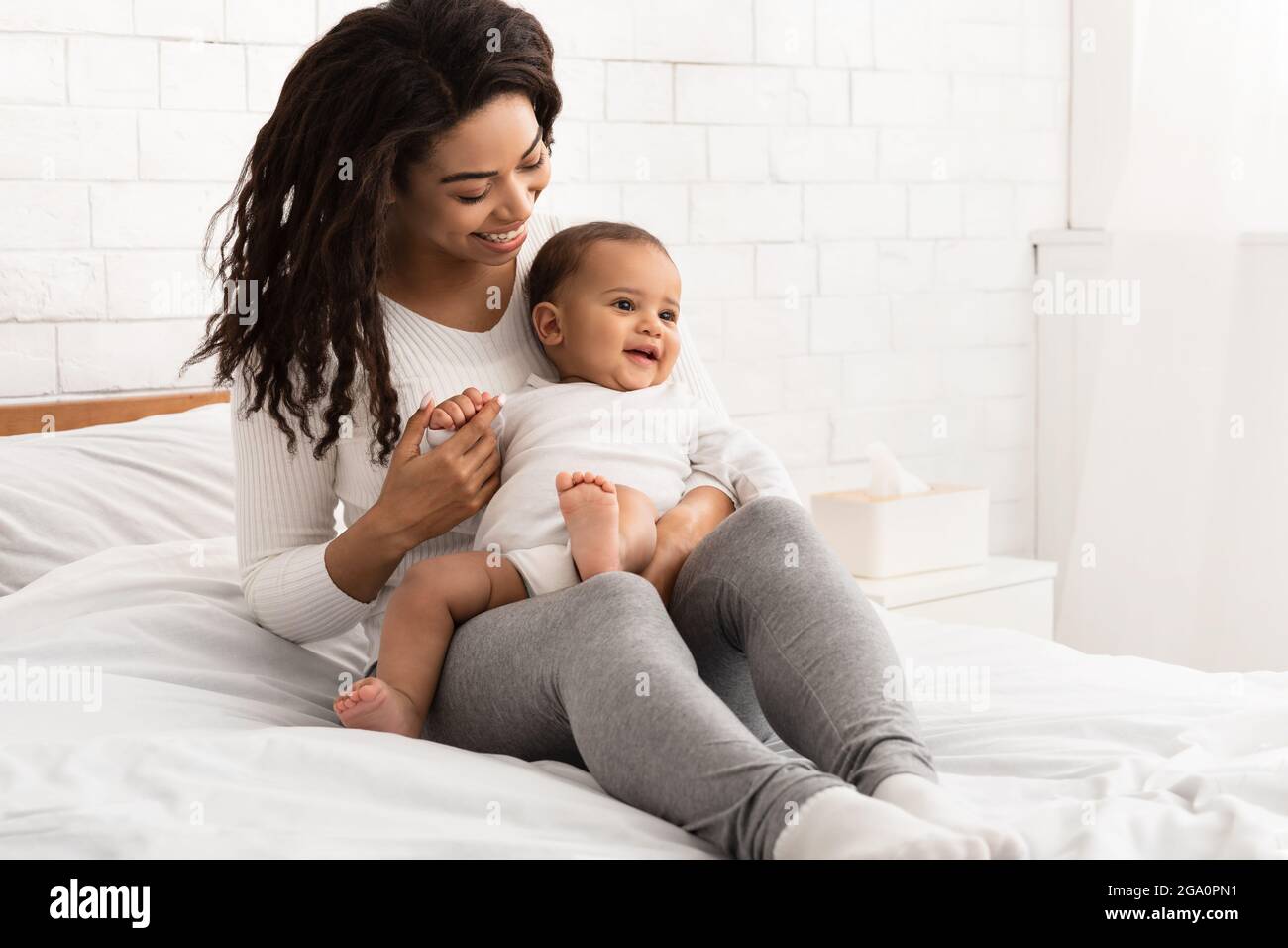 Black Mom Playing With Infant Baby Sitting In Bed Indoor Stock Photo