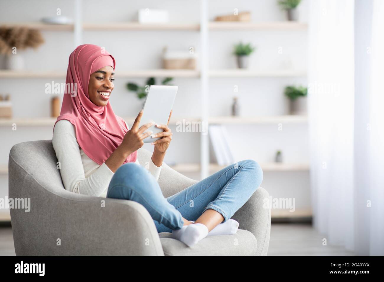 Young Black Muslim Woman In Hijab Relaxing In Chair With Digital Tablet ...