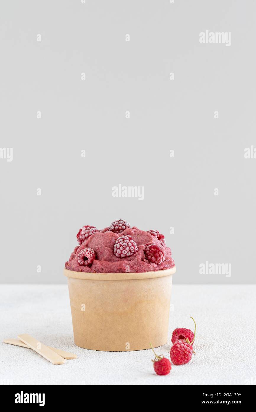 Red raspberry and banana vegan ice cream with frozen raspberries in paper bowl Stock Photo