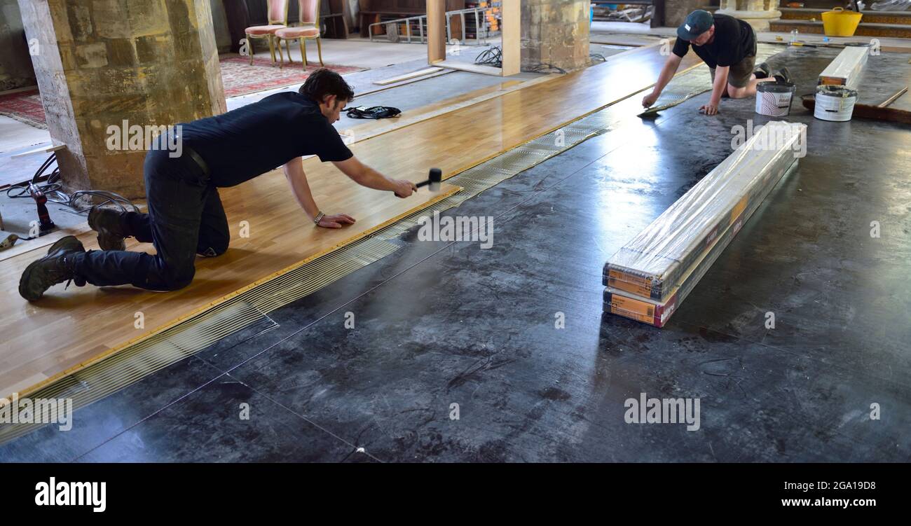Workman installing laminate wooden tongue and groove flooring one spreading adhesive when other taps down boards Stock Photo
