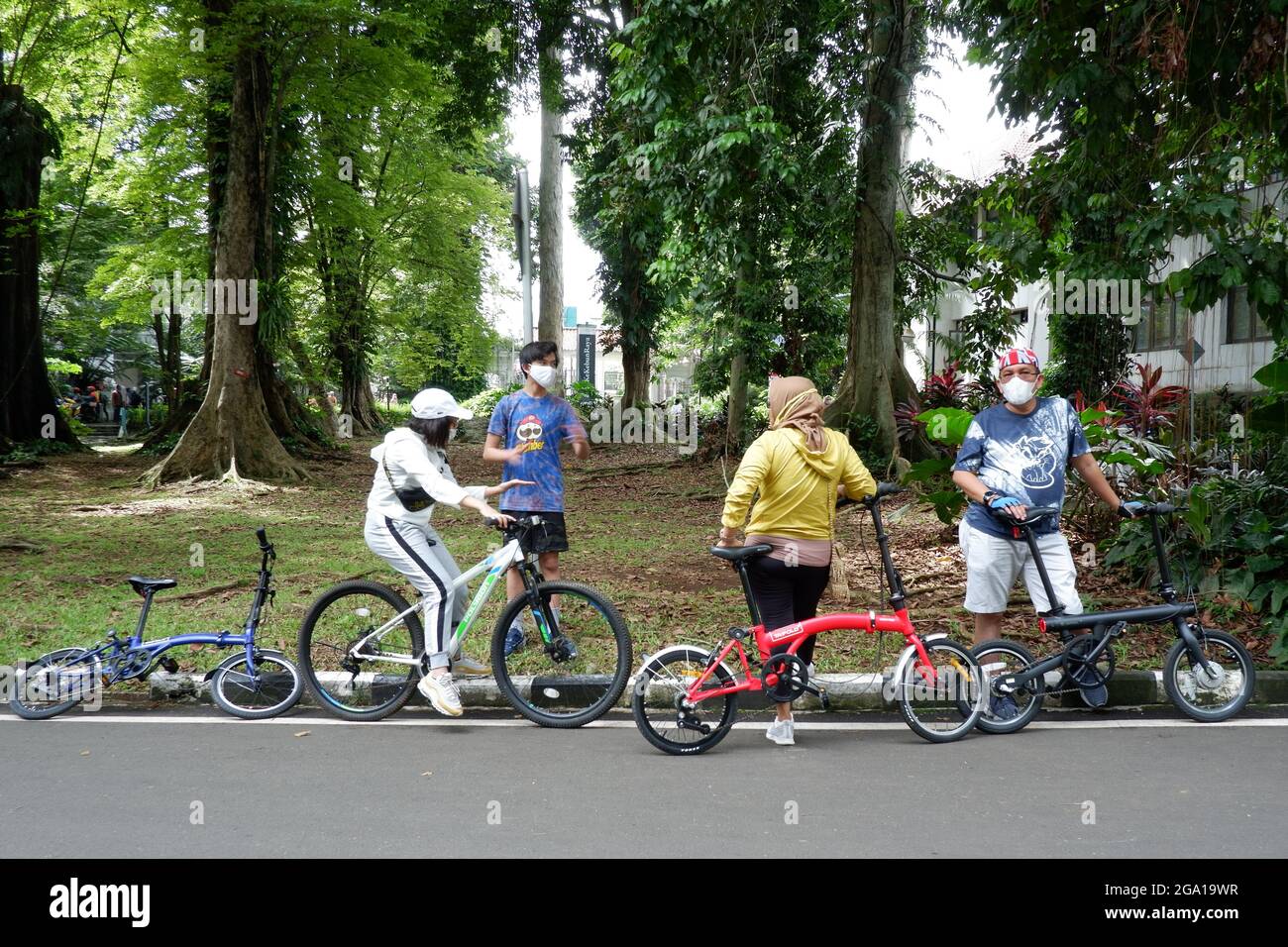 A family with facemask and bikes rest on street side. Stock Photo