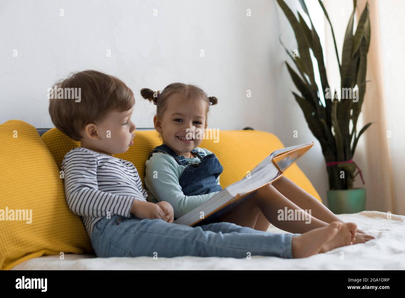 Two preshool, toddler children read large interesting book of fairy tales on yellow bed. Siblings little twins reader have fun, happy kid on Stock Photo