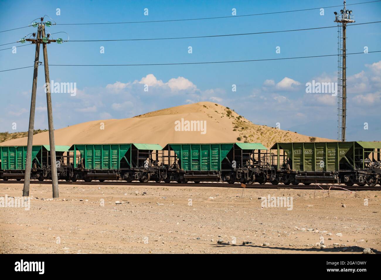 Altynkol, Kazakhstan - June 05, 2012: Railway station Altynkol. Hopper cars train on yellow sand dune and blue sky with clouds backdrop. Stock Photo