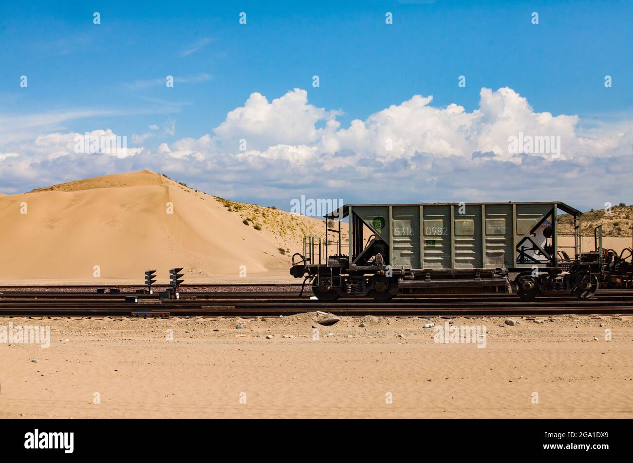 Altynkol, Kazakhstan - June 05, 2012: Railway station Altynkol. Hopper car on yellow sand dune and blue sky with clouds backdrop. Stock Photo