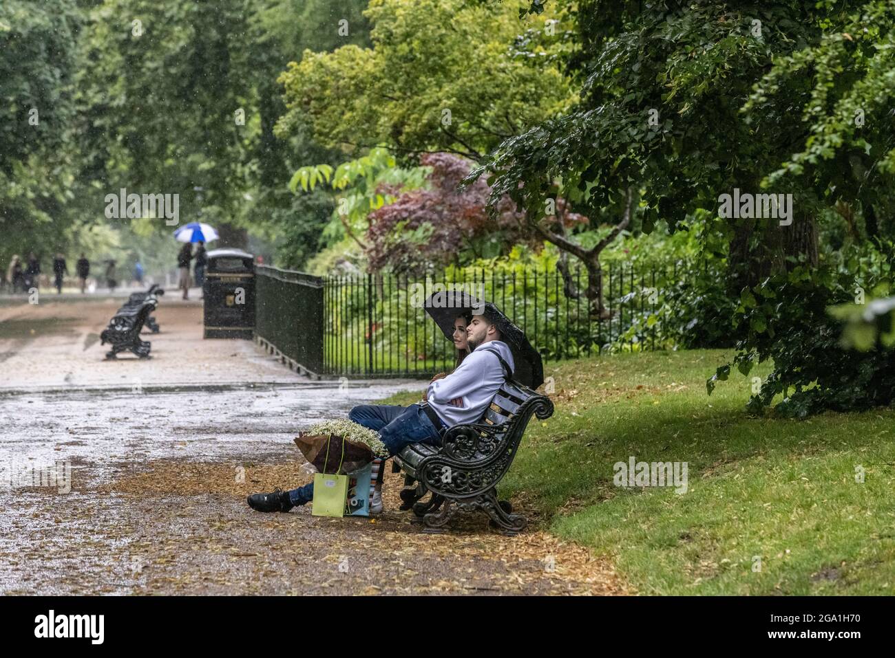 London, UK. July 28 2021: London, UK. July 28 2021: Heavy Rain Showers, Central London, England, UK Picture shows a couple taking cover underneath their umbrella from the rain in Hyde Park as heavy rain showers sweep across Central London and southern parts of England. Credit: Clickpics/Alamy Live News Stock Photo