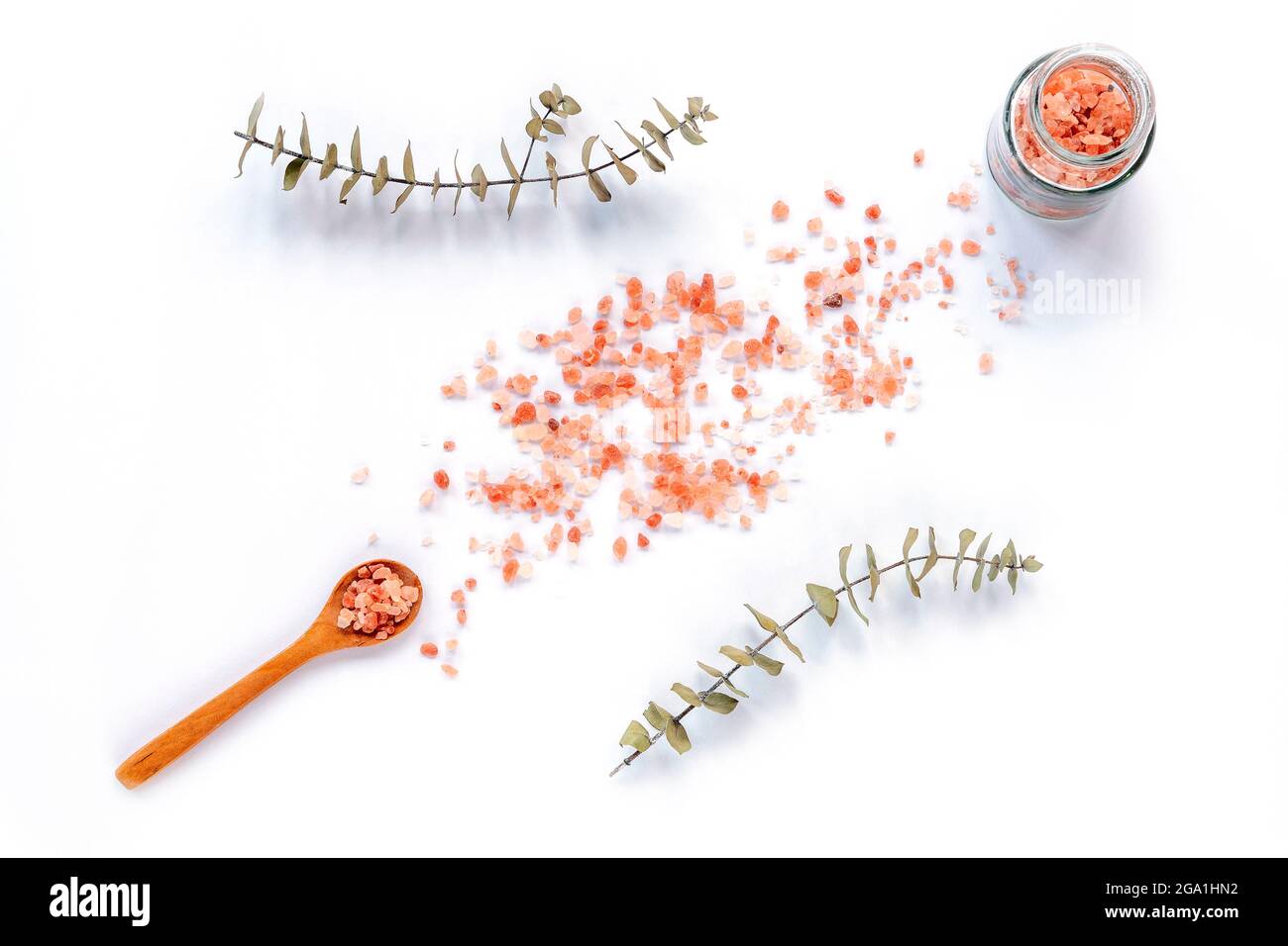 Himalayan pink salt in glass jar and wooden spoon isolated on white background. Eucalyptus leaves as decoration, top view. Stock Photo