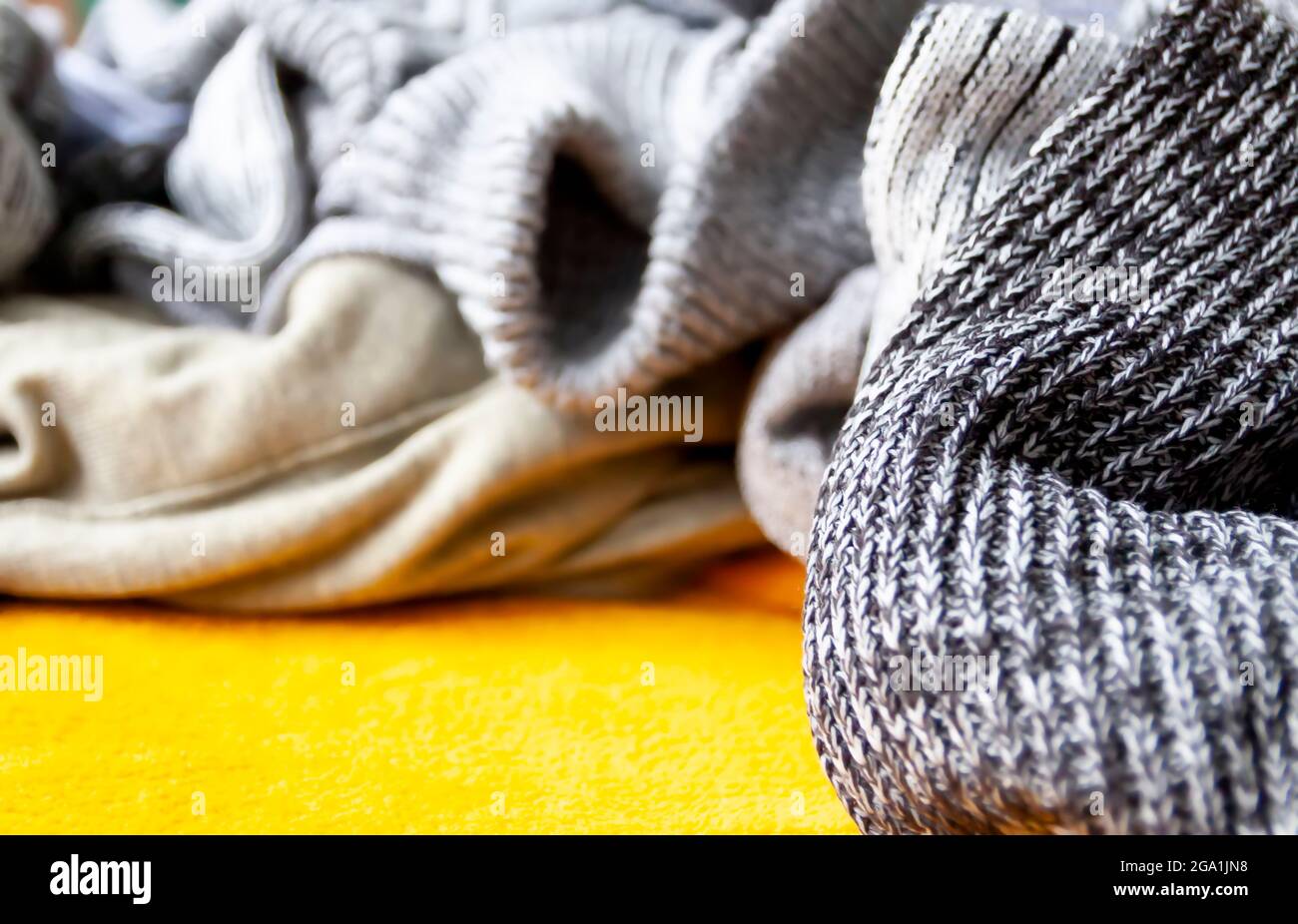 Warm knitted jumpers and sweaters on bright yellow background. Stock Photo