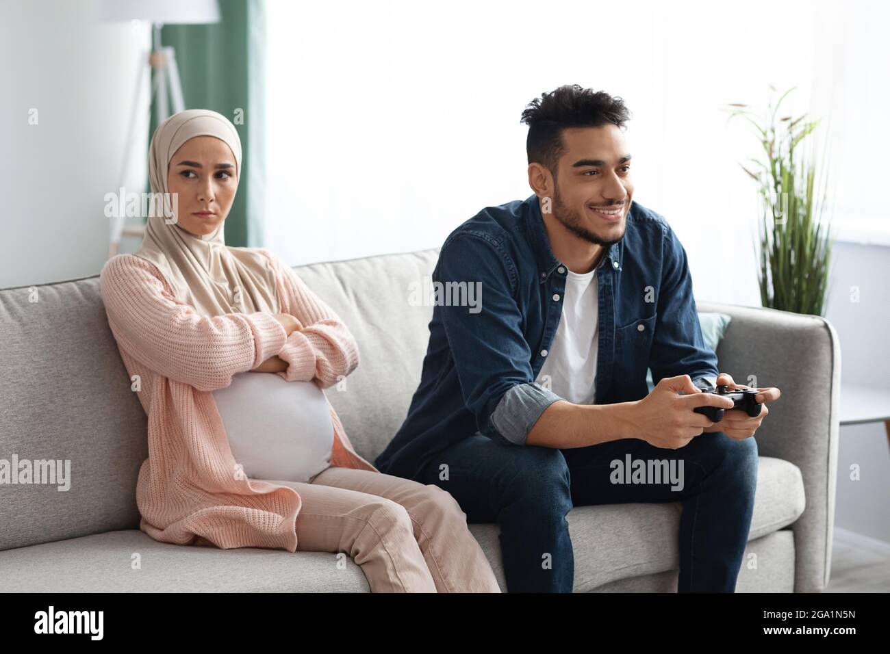 Upset Expectant Muslim Woman Sitting Offended To Husband That Playing Video Games Stock Photo