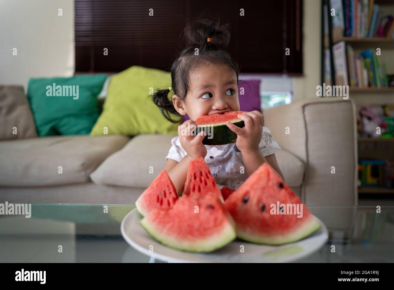 Shallow focus shot of a little Thai girl eating watermelon Stock Photo