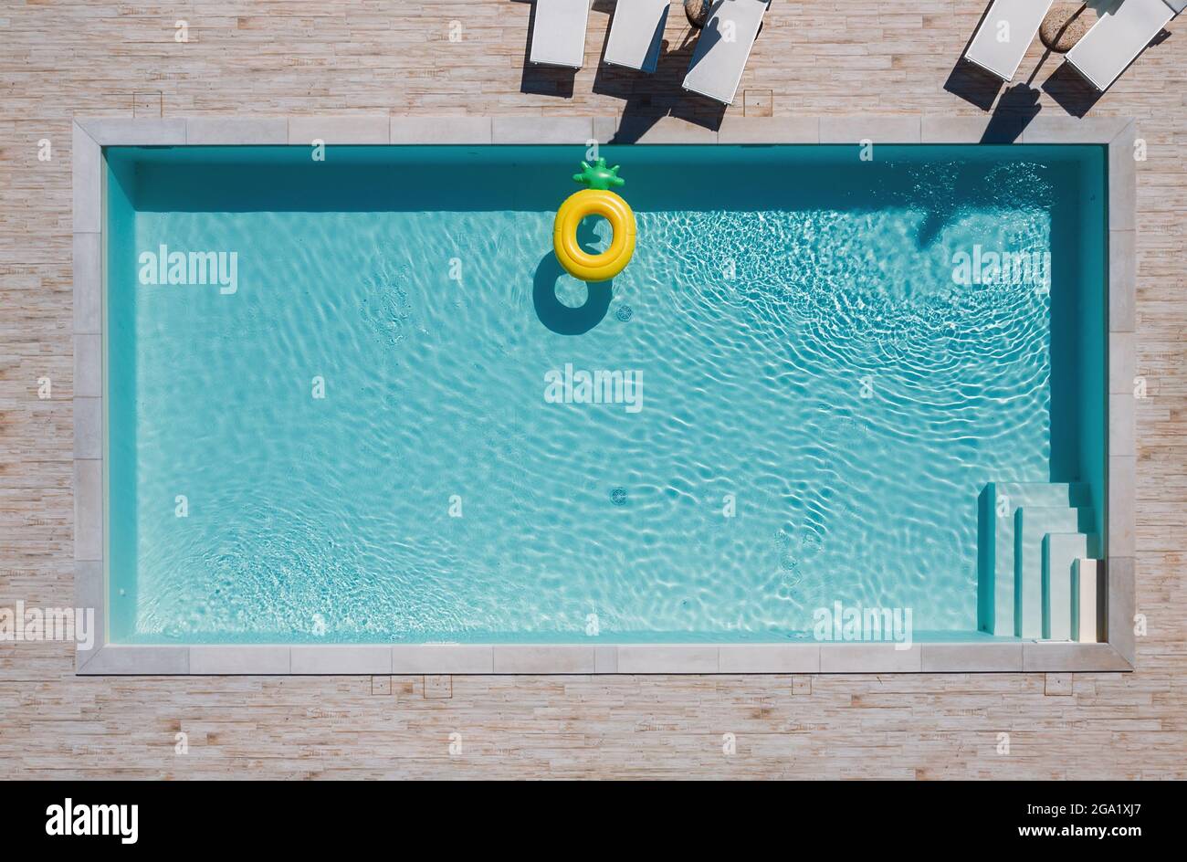 Empty rectangular blue swimming pool with sunbeds and umbrellas and big inflatable Yellow Pineapple floating tube. Rent a real estate or Chill out sum Stock Photo