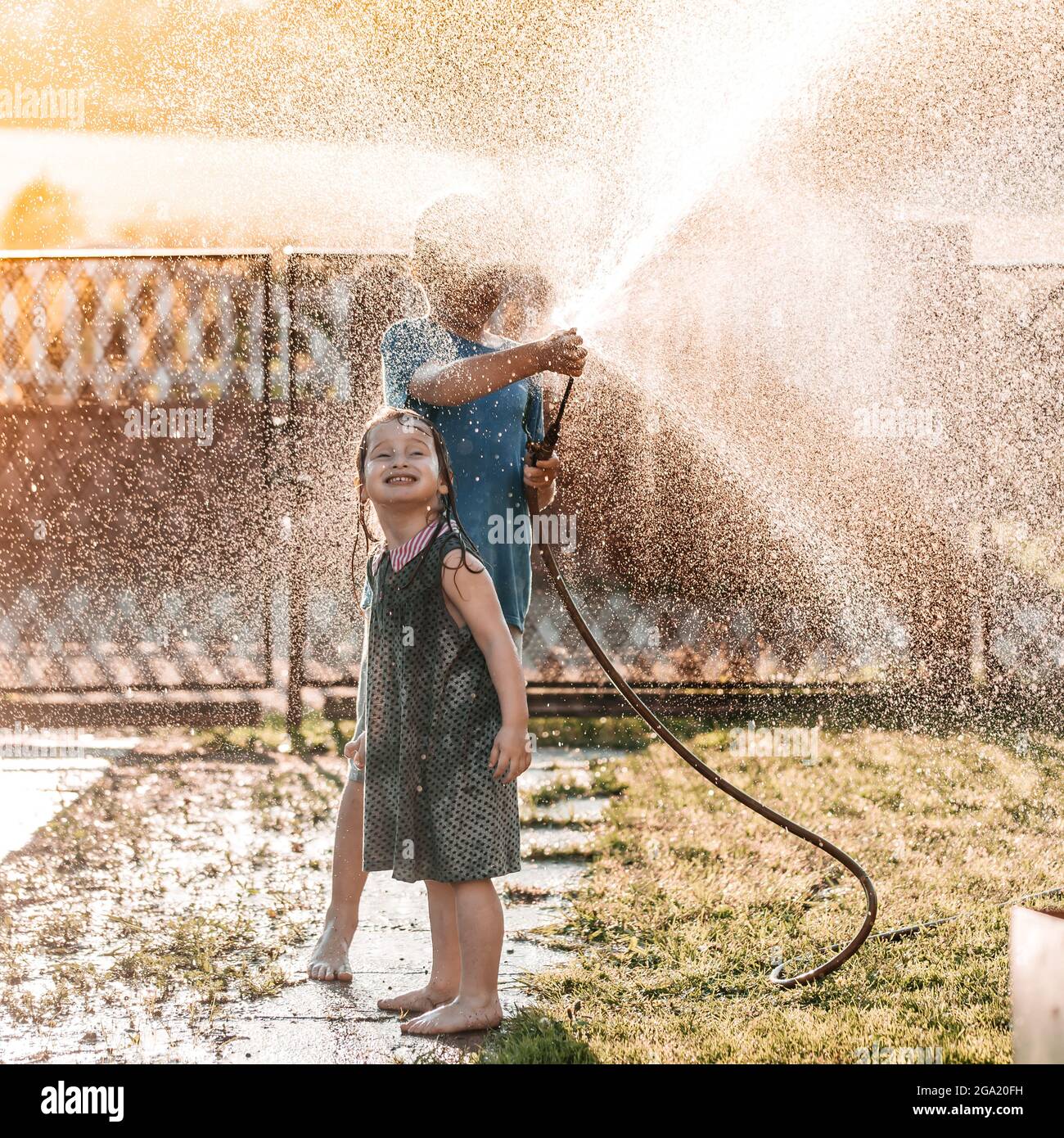 little children playing together with a garden hose on hot and sunny summer day on sunset Stock Photo