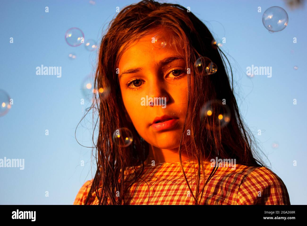 Beautiful teenage girl amidst soap bubbles flying in the air at a sunset. Portrait of a 10-12 years old kid. Schoolgirl on summer holiday. Entertainme Stock Photo
