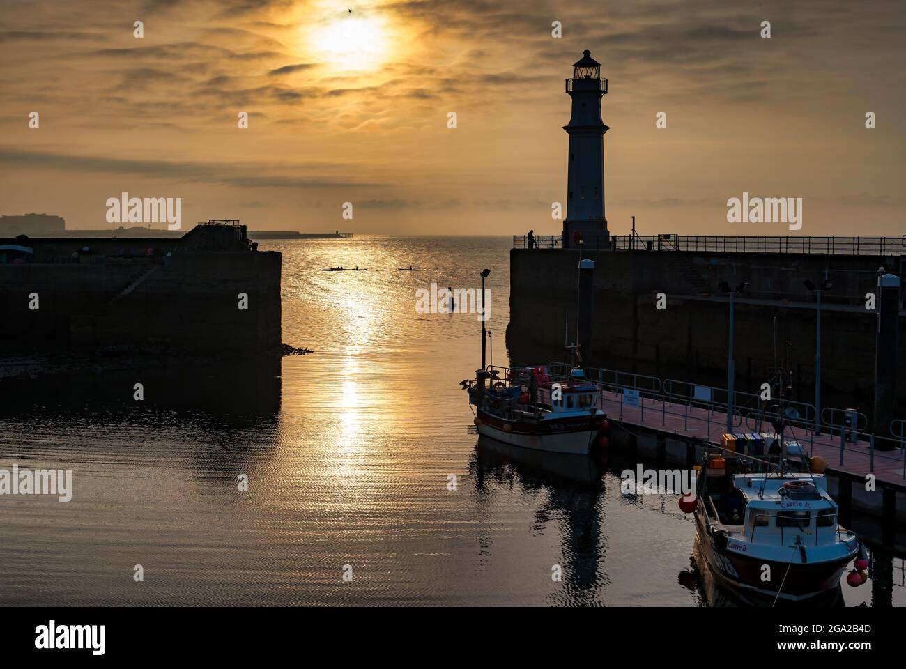 Boats in Newhaven harbour with lighthouse and kayakers at sunset, Firth of Forth, Edinburgh, Scotland, UK Stock Photo