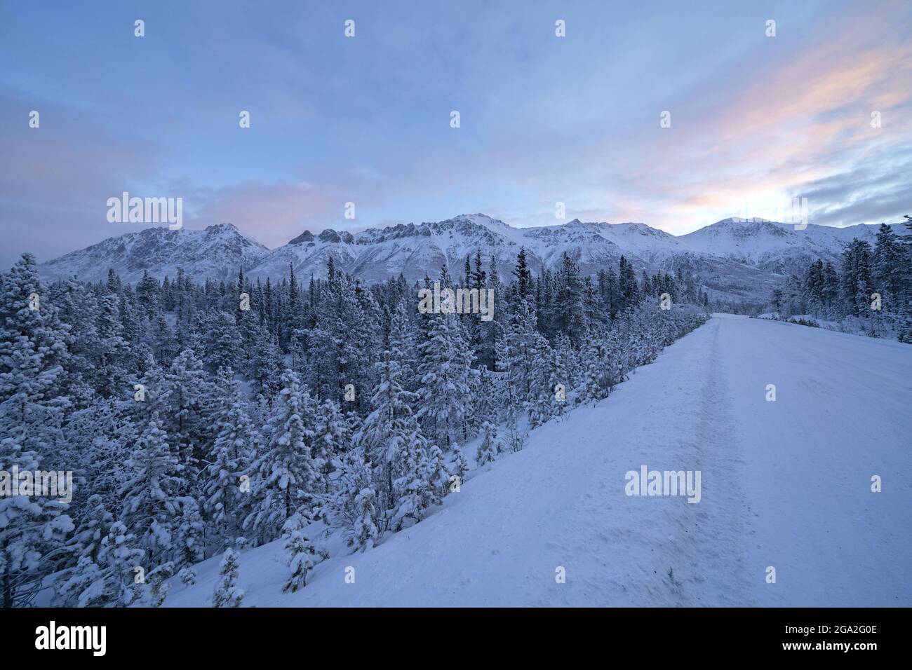 The Alaska Highway stretching into the distance with the morning light rising behind the snowy mountaintops; Whitehorse, Yukon, Canada Stock Photo