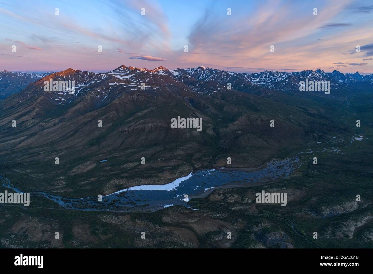 Aerial view of the dramatic mountain ranges and a river running through the tundra along the Dempster Highway at sunset; Yukon, Canada Stock Photo