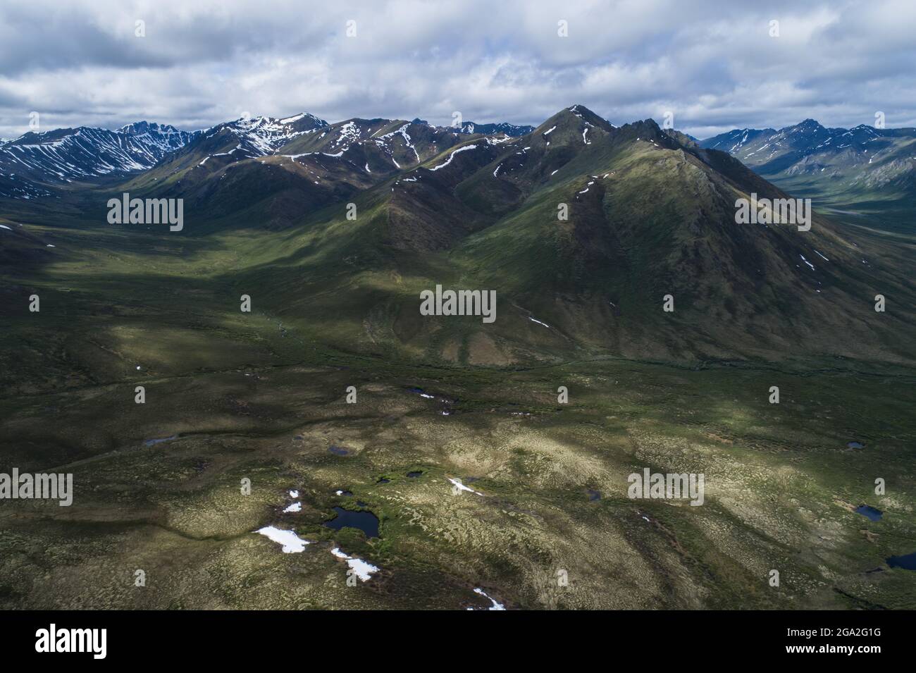 Aerial view of the mountain ranges covered in a blanket of green vegetation in the summer along the Dempster Highway; Yukon, Canada Stock Photo
