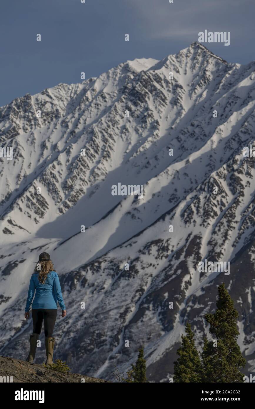 View from behind of a woman standing on mountainside looking at the close-up view of a majestic snowcapped mountain, situated in the Traditional Te... Stock Photo