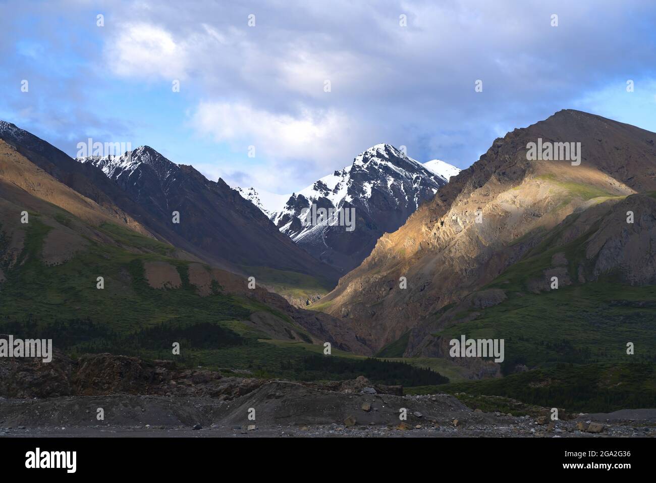 The landscape of Kluane National Park with mountain slopes covered in green vegetation and snowcapped mountain peaks on the horizon. An amazing pla... Stock Photo
