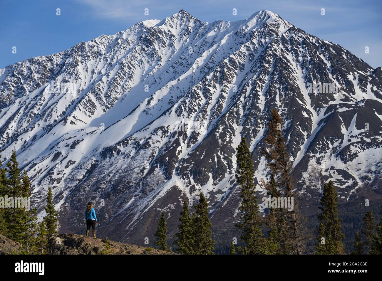 View from behind of a woman standing on mountainside looking at the imposing view of a majestic snowcapped mountain, situated in the Traditional Te... Stock Photo