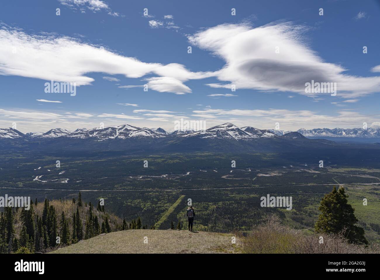 View from behind of a woman standing on mountaintop looking out at the vista of the majestic snowcapped mountain ranges, situated in the Traditiona... Stock Photo