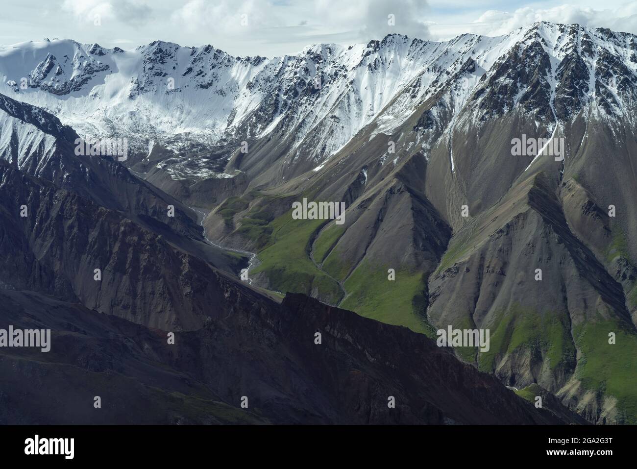 Aerial of slopes of ancient sedimentary and volcanic rock with green vegetation and snowcapped mountain peaks on the horizon, situated in the Tradi... Stock Photo
