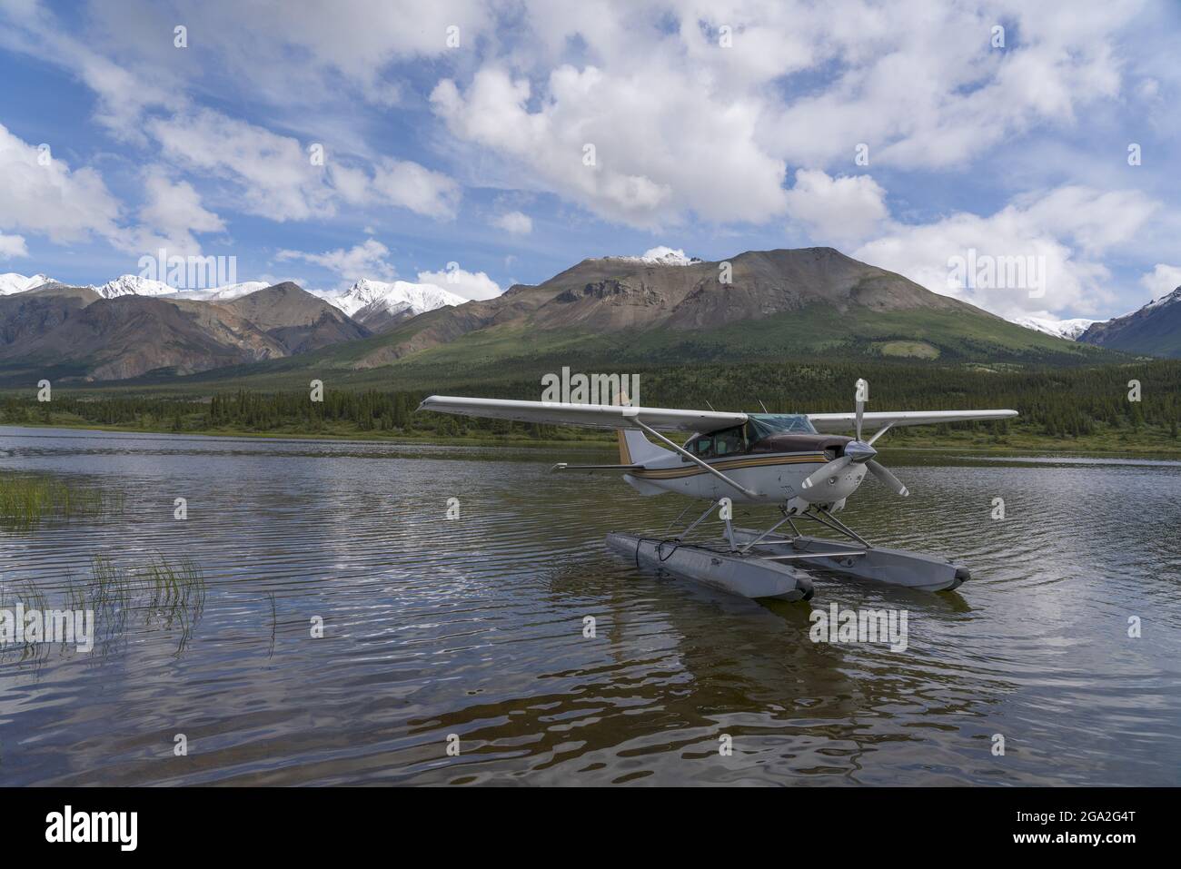 Floatplane on the water resting near the shore of a lake with mountains in the background; Kluane National Park and Reserve, Yukon, Canada Stock Photo