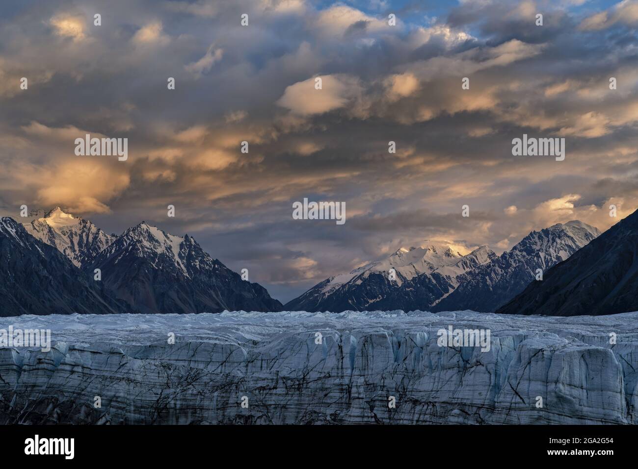 The vast Donjek Glacier in Kluane National Park with the sunset lighting up the clouds over the snowcapped mountaintops creating a stunning image, ... Stock Photo