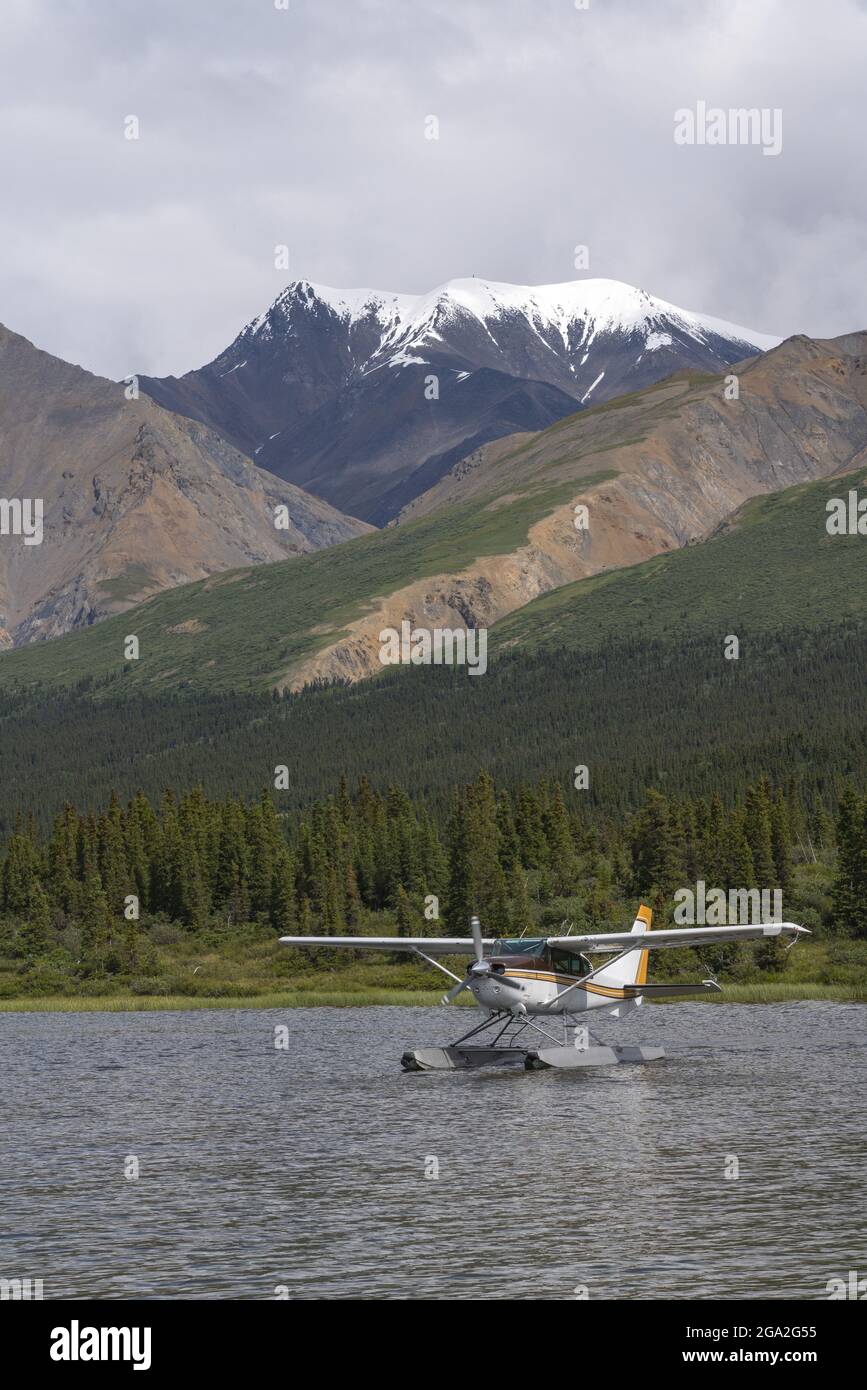 Floatplane on the water resting near the shore of a lake with forested and snowcapped mountains in the background Stock Photo