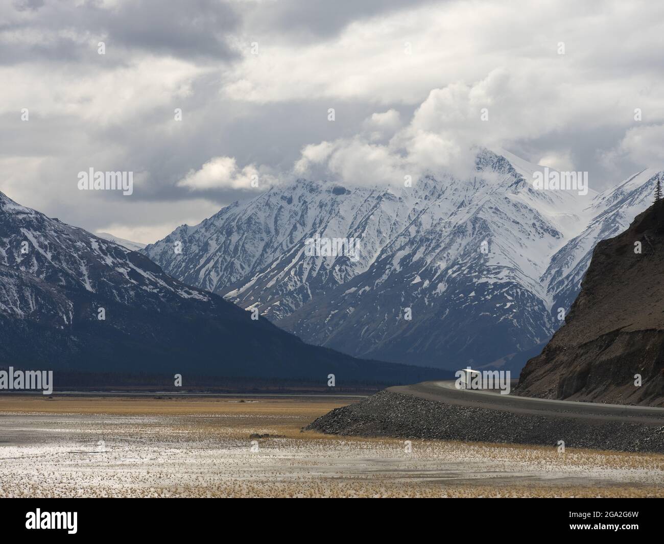 Transport truck driving the Alaska Highway along side the dried up portion of Kluane Lake with huge mountains in the distance, situated in the Trad... Stock Photo