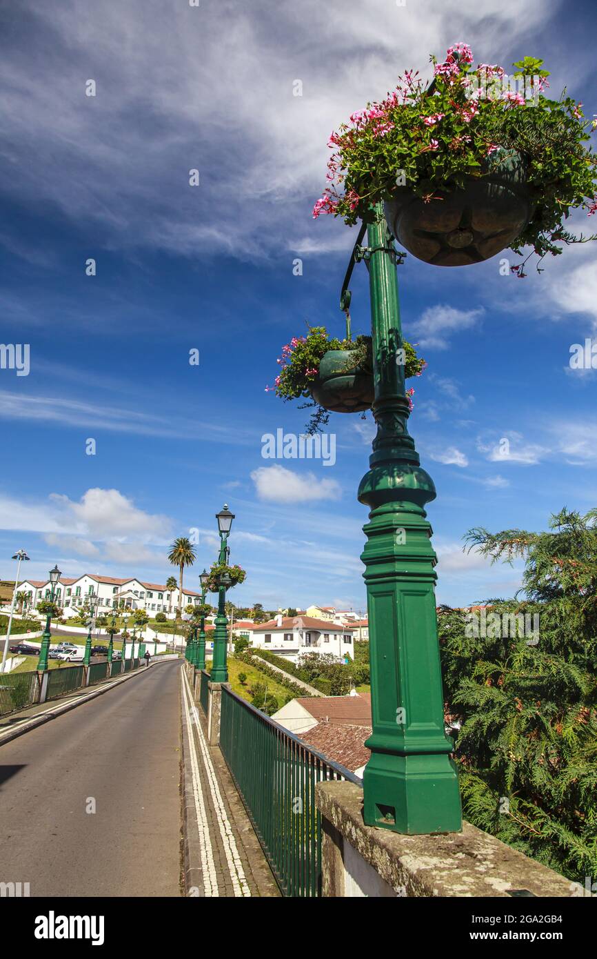 Lampposts filled with flowering planters line the road and historical bridge in the picturesque town of Nordeste; Sao Miguel Island, Azores Stock Photo