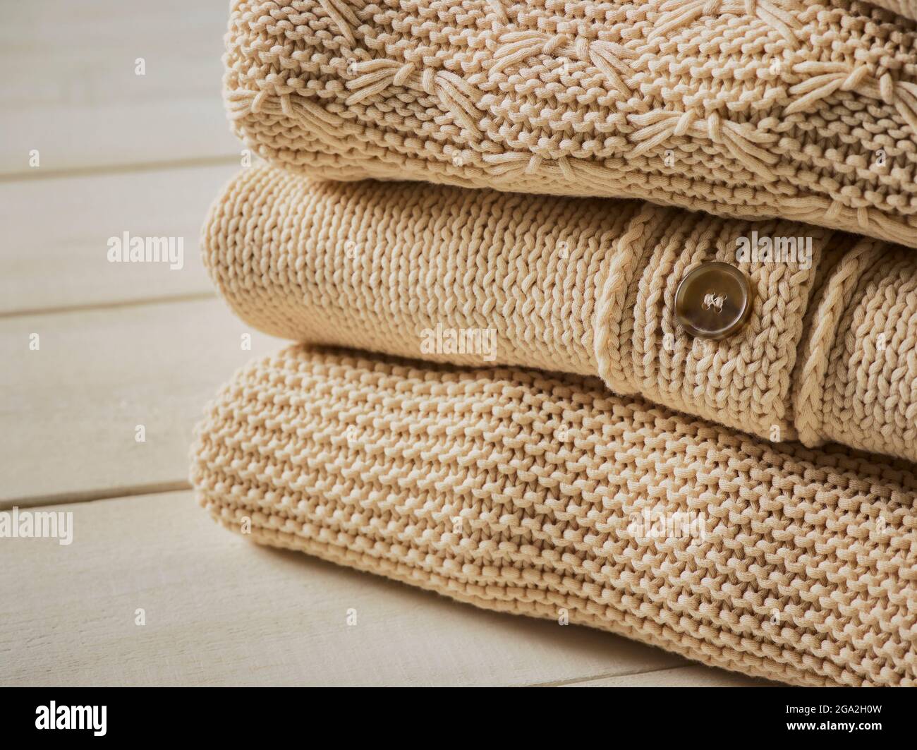 Three beige knit sweaters folded in a pile; Studio Stock Photo