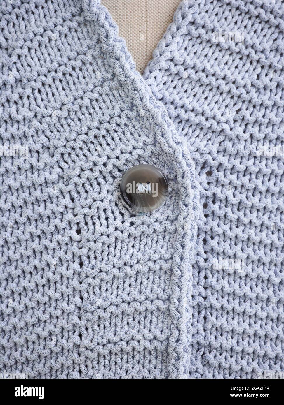Extreme close-up of the collar and button on a grey knit sweater on a mannequin; Studio Stock Photo