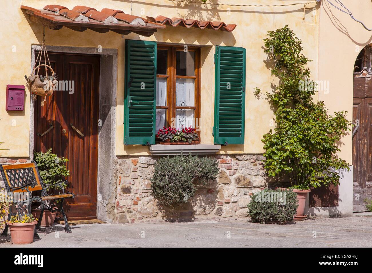 Traditional stucco home with wooden front door and window with green shutters on a sunny day in the town of Cortona; Arezzo, Tuscany, Italy Stock Photo