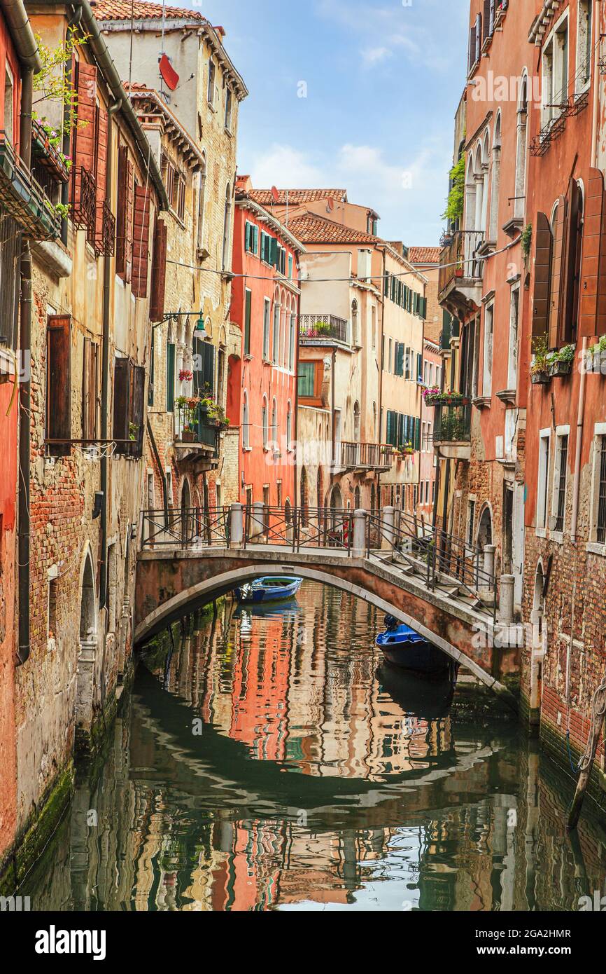 Small foot bridge spanning a side canal in-between colorful stone buildings; Venice, Venezia, Italy Stock Photo