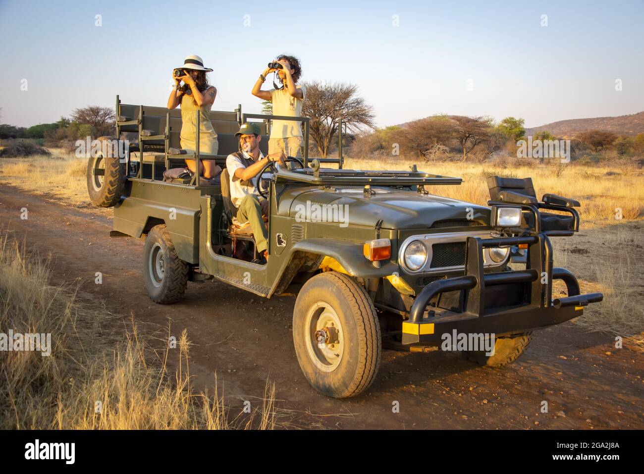 Women in a jeep, one using binoculars and one using a camera, looking into the savanna with a driver sitting behind the wheel while on safari at th... Stock Photo