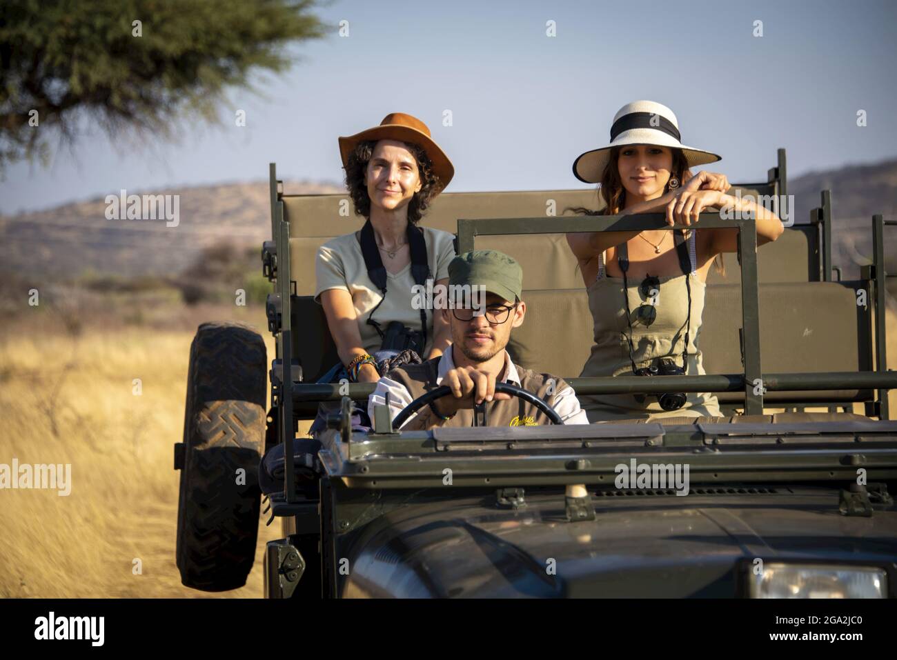 Women sitting in the back seat of a jeep on safari with a guide driving them through the savanna, looking at camera at the Gabus Game Ranch Stock Photo
