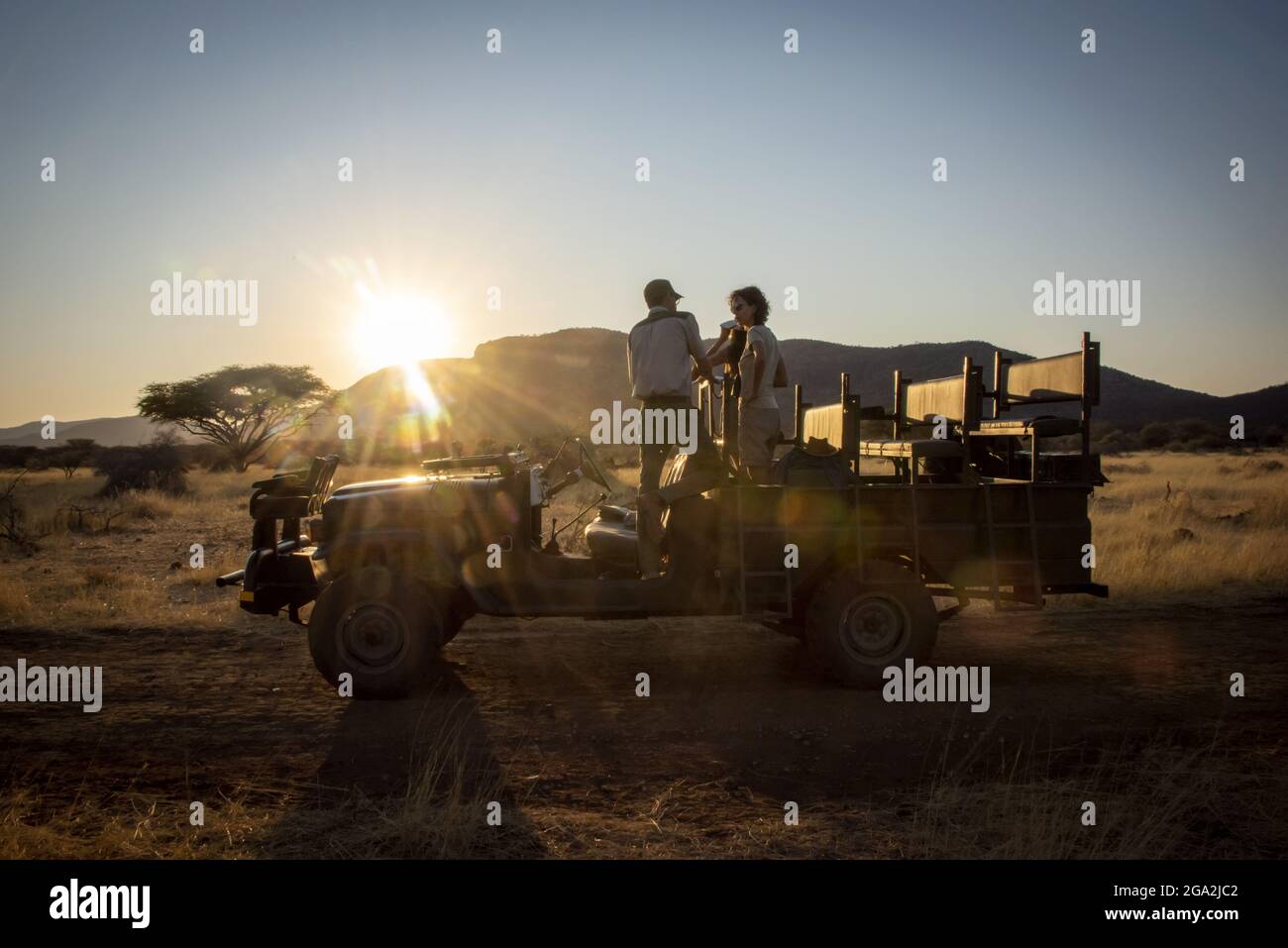 Safari guide speaking with guests while standing in a jeep on the savanna at the Gabus Game Ranch at sunrise; Otavi, Otjozondjupa, Namibia Stock Photo