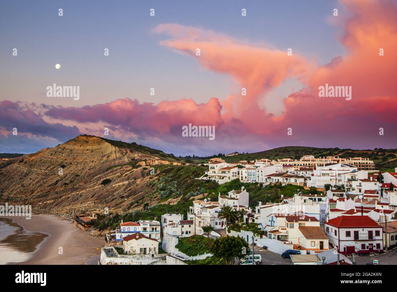 Dramatic pink cloud formation and full moon in a blue sky above the traditional fishing village of Burgau in the municipality of Vila do Bispo in t... Stock Photo