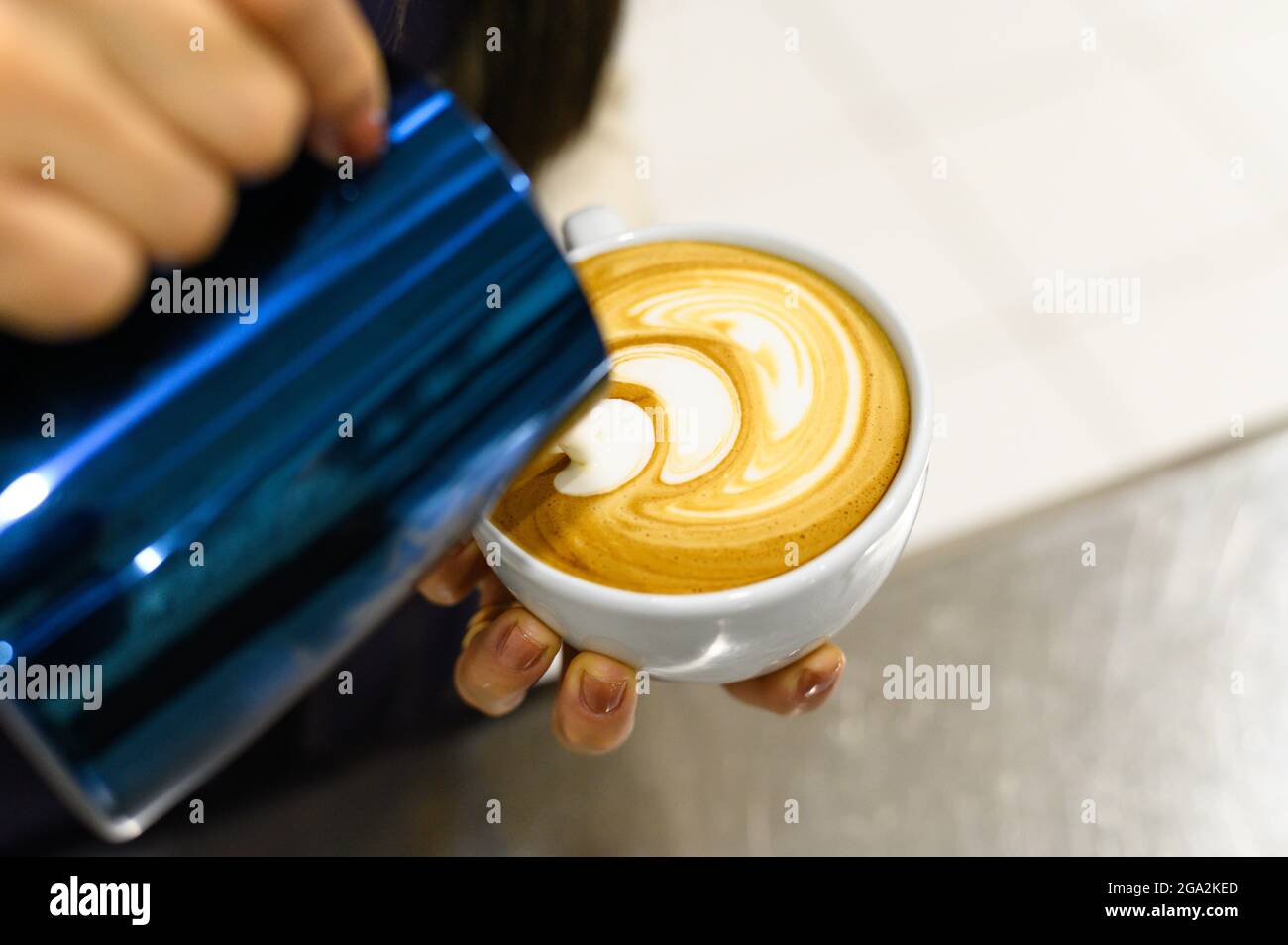 Hands of barista making latte or cappuccino coffee pouring milk, making latte art. Stock Photo