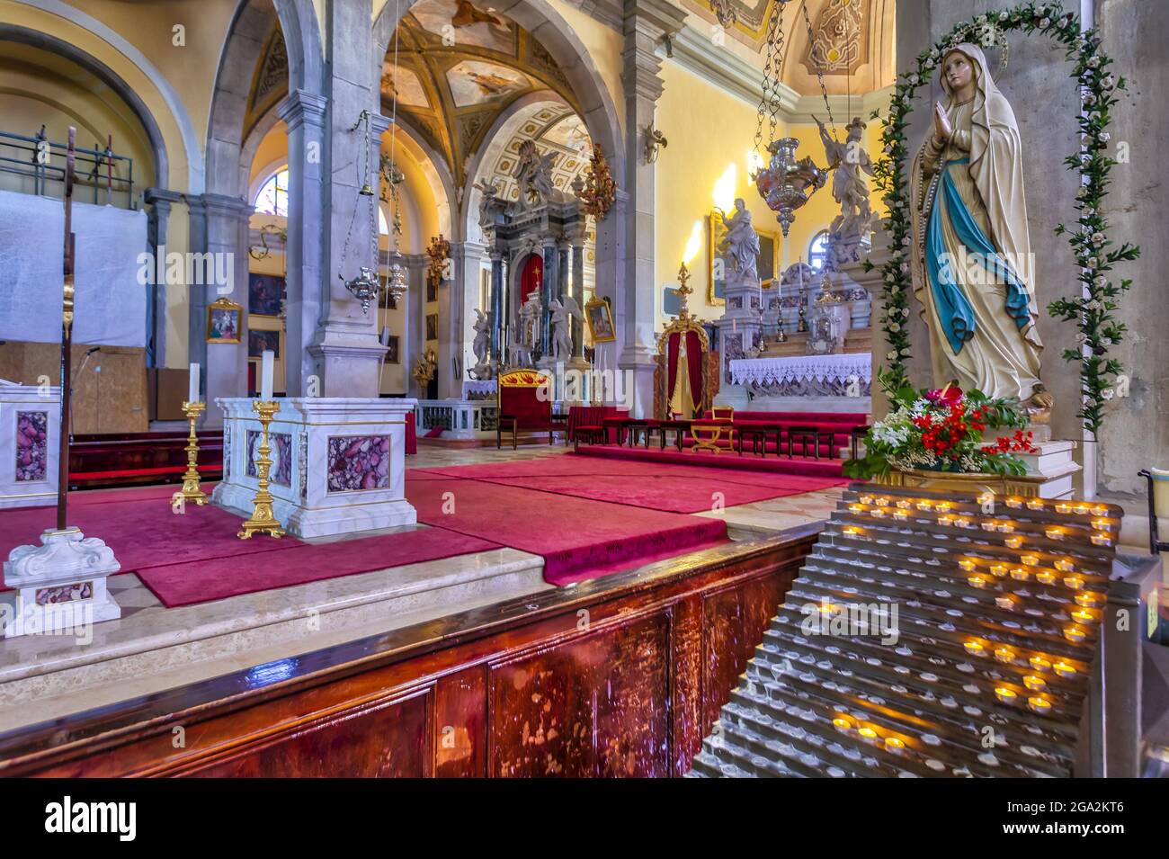 Interior of the Church of St Euphemia, showing a religious statue and candles lit for prayers and intentions with an elaborate main altar in the ba... Stock Photo