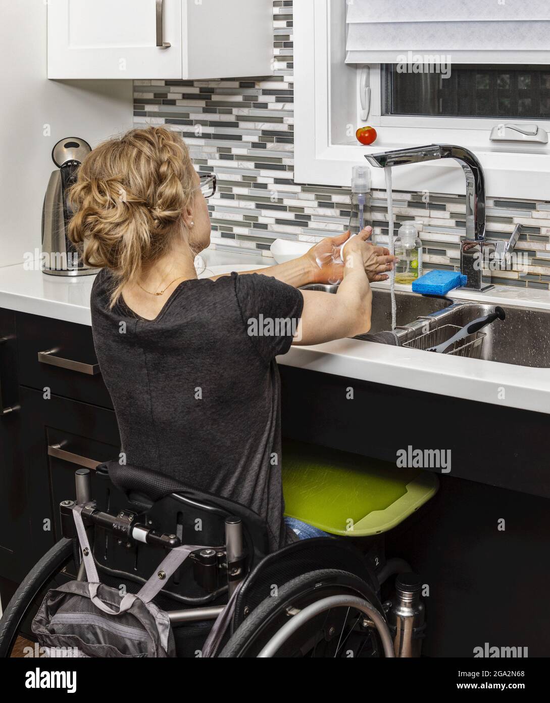 A paraplegic woman washing her hands at the sink while preparing a meal from her wheelchair; Edmonton, Alberta, Canada Stock Photo