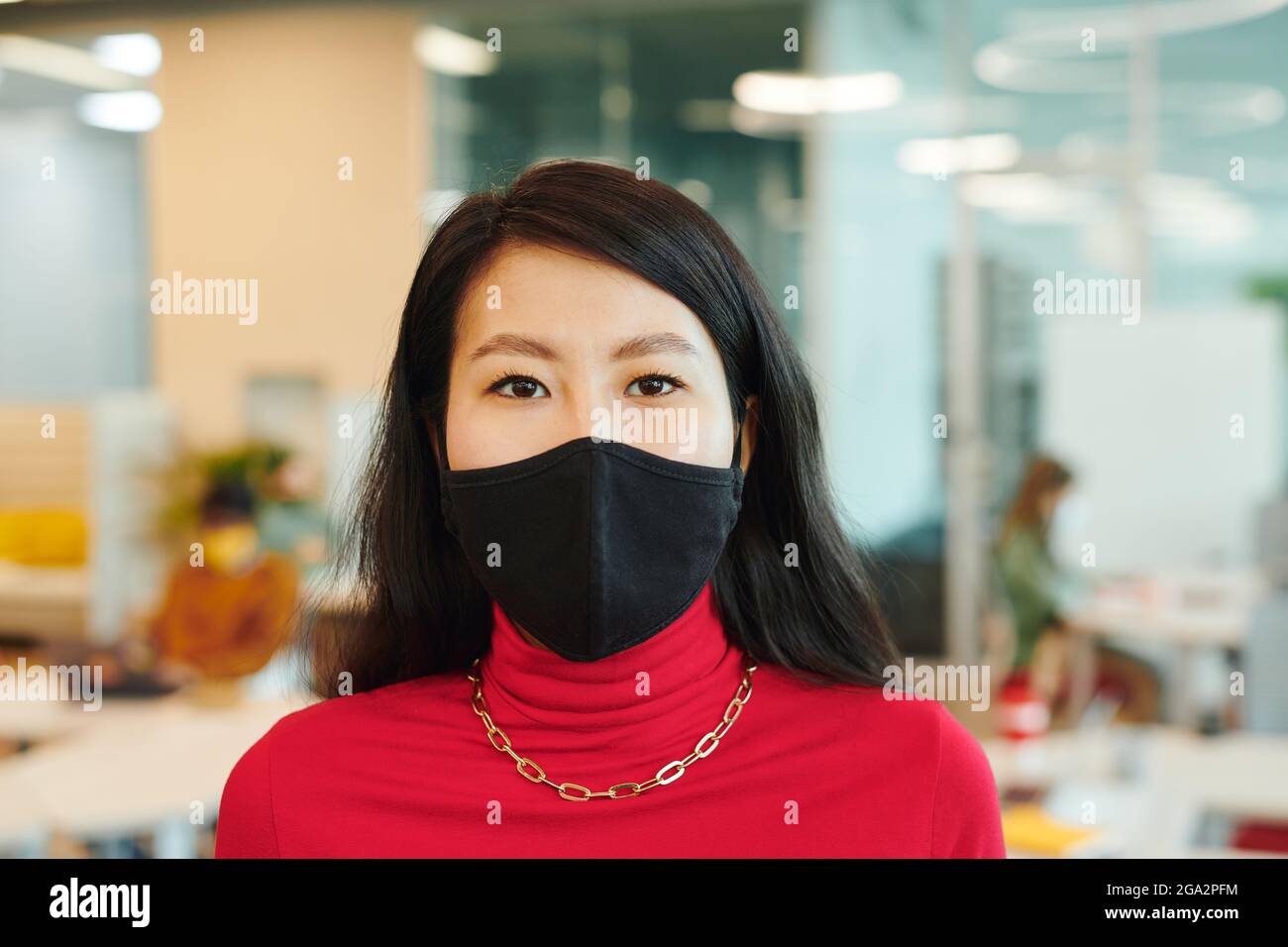 Young female office manager of Asian ethnicity looking at you while standing in front of camera in open space environment Stock Photo