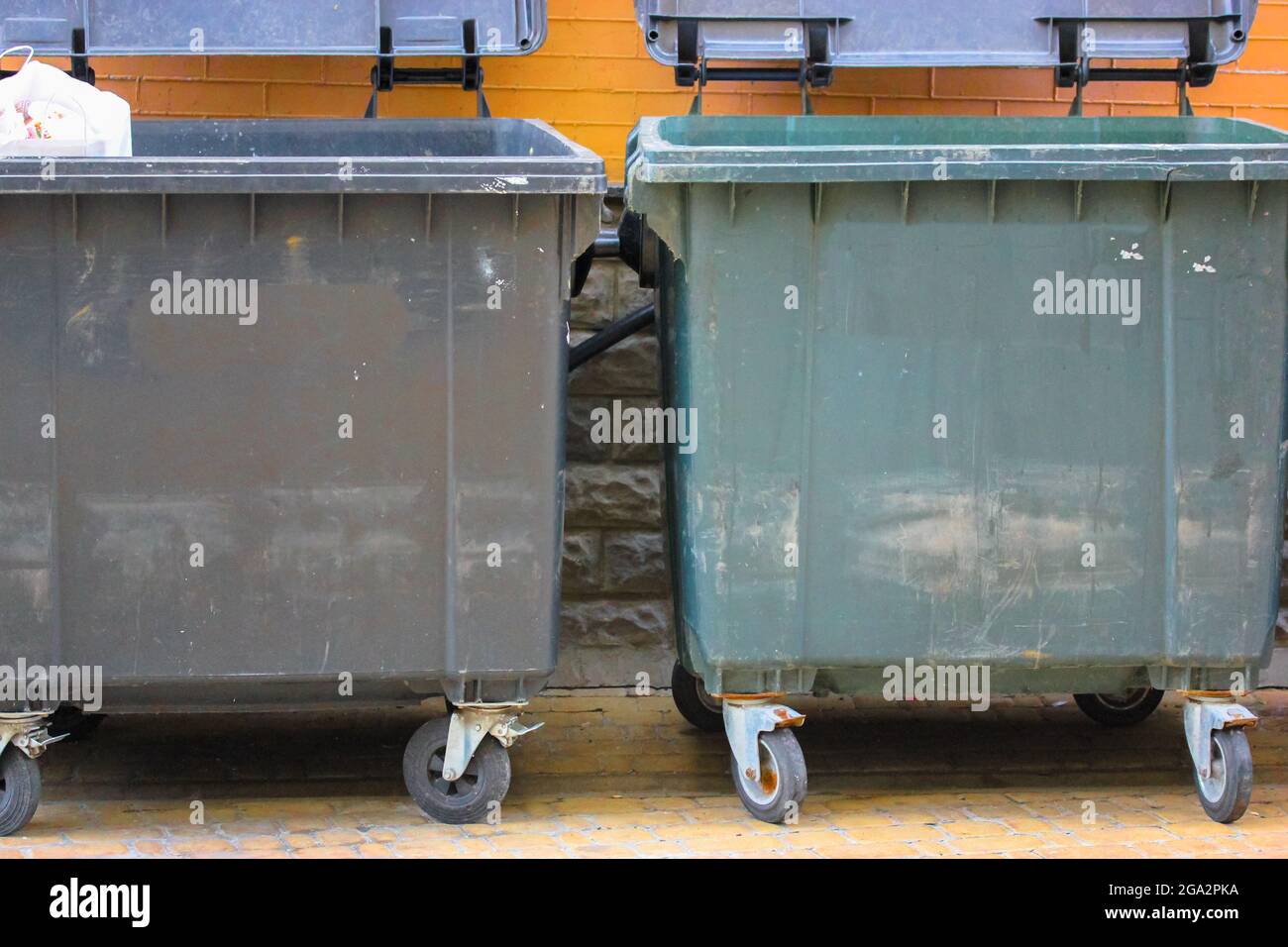 Plastic large trash cans with the lids up and garbage inside against a  brick orange wall. Big green and grey plastic dumpsters on a city street.  Waste Stock Photo - Alamy