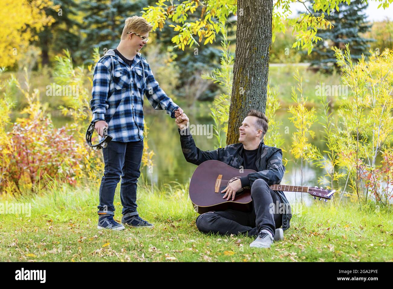 A young man with Down Syndrome does a fist bump after playing a tambourine while his father played a guitar in a city park on a warm fall evening Stock Photo