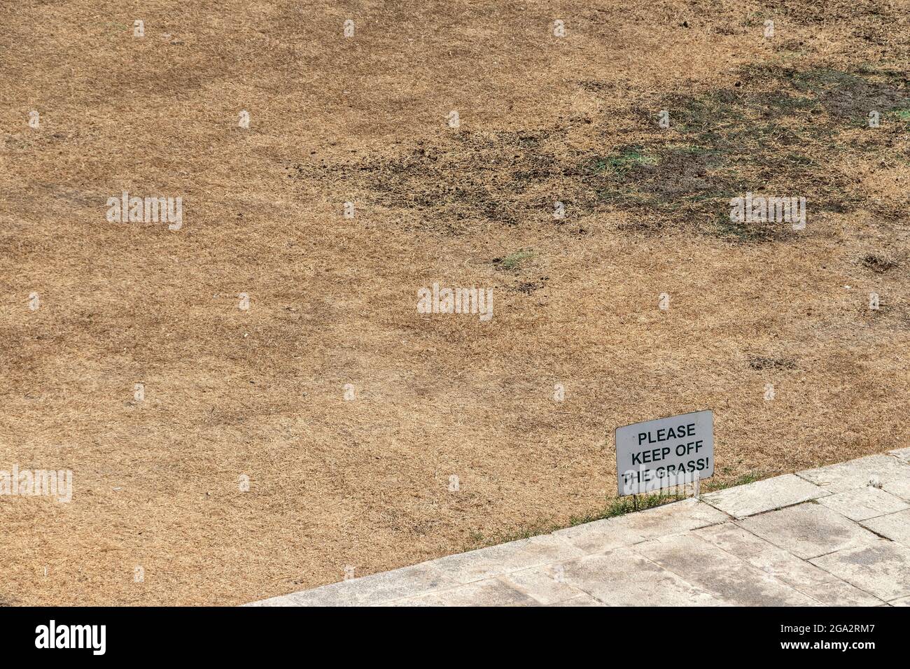 Badly sun burnt grass area with sign saying 'Please Keep Off The Grass'. Malta. Stock Photo