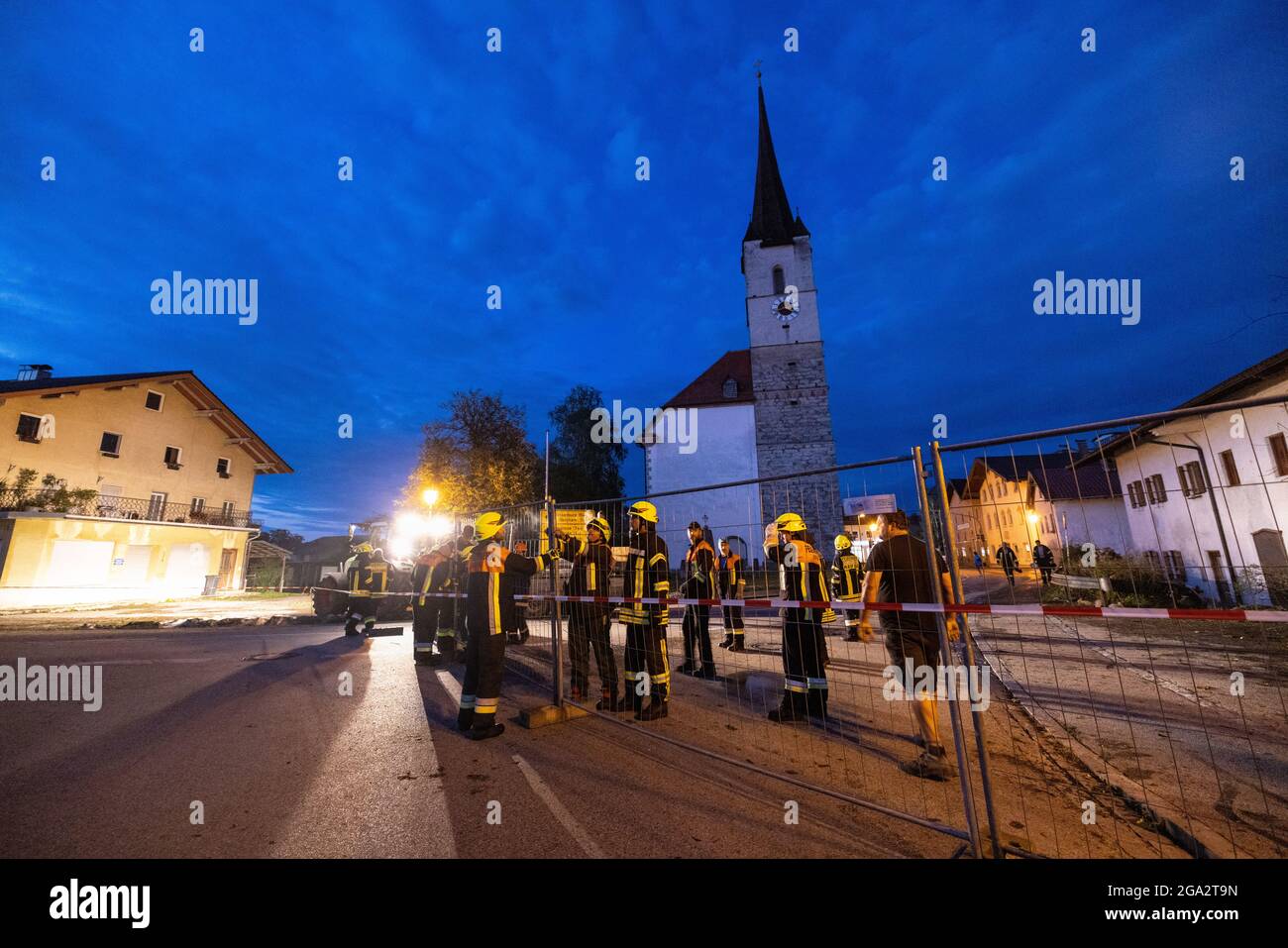 Halfing, Germany. 28th July, 2021. Firefighters use a fence to block off the road in front of Halfing's church tower, which was so badly damaged by a storm that structural engineers have to check whether the tower is in danger of collapsing. A violent storm had passed over the region shortly before. Credit: Matthias Balk/dpa/Alamy Live News Stock Photo