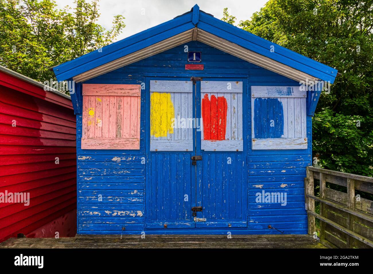 Weather worn beach hut at Whitstable, Kent. Blue with painted square panels in light blue, red, yellow and pink. Stock Photo