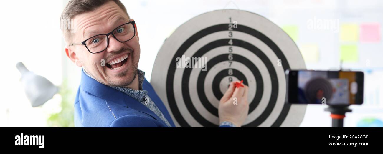 Businessman playing darts in front of mobile phone camera Stock Photo